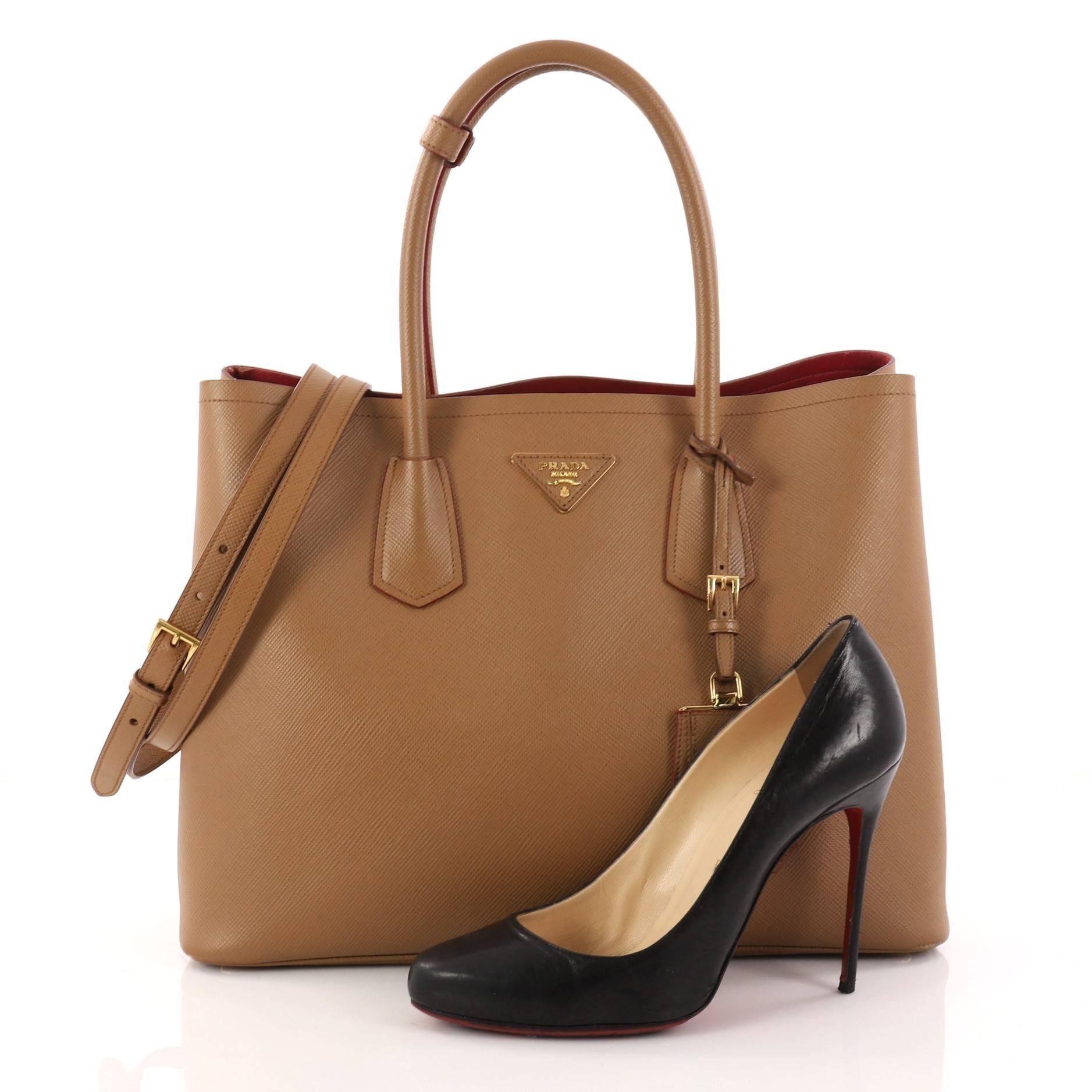 This authentic Prada Cuir Double Tote Saffiano Leather Medium is elegant in its simplicity and structure. Crafted from brown saffiano leather, this tote features dual-rolled handles, side snap buttons, Prada's trademark triangle logo at the center,
