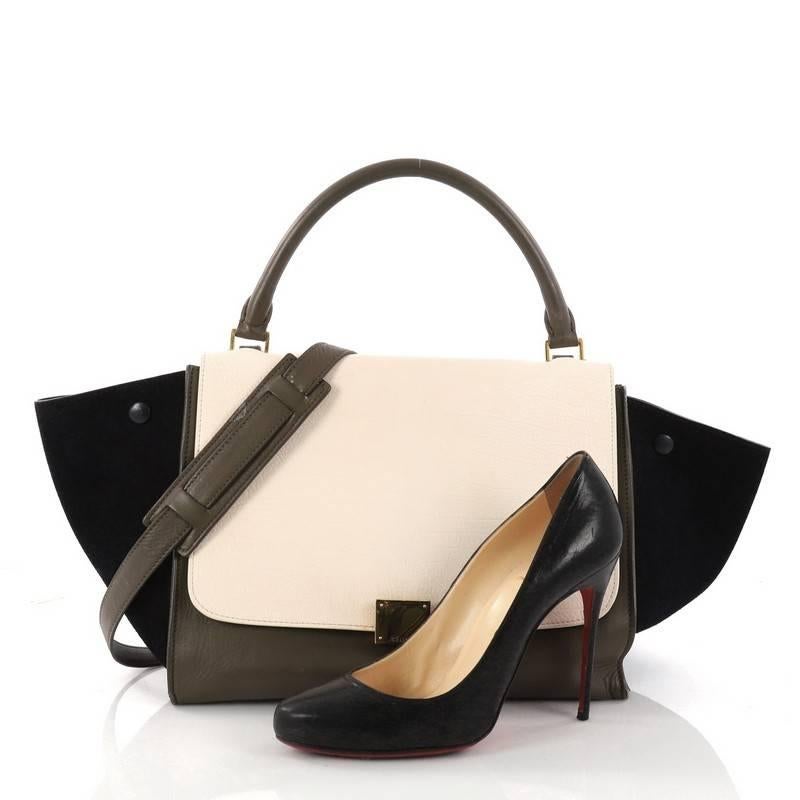 This authentic Celine Tricolor Trapeze Handbag Leather Small is a modern minimalist design with a playful twist in an array of subdued colors. Crafted from off-white and olive green leather and navy suede wings, this classic satchel features