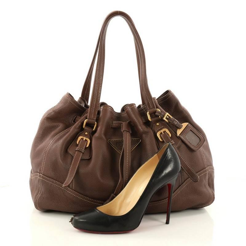 This authentic Prada Drawstring Tassel Tote Cervo Leather is an excellent tote, ideal for everyday use. Crafted in brown cervo leather, this stylish tote features dual flat leather handles with belt and buckle details, leather cinch strap running