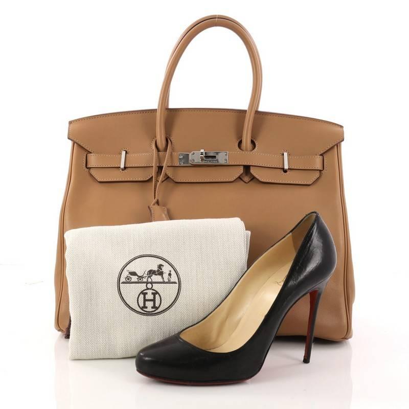 This authentic Hermes Birkin Handbag Tabac Brown Swift with Palladium Hardware 35 showcases subtle elegance. Finely crafted in beautiful tabac brown swift leather, this piece features dual-rolled top handles, frontal flap, turn-lock closure,