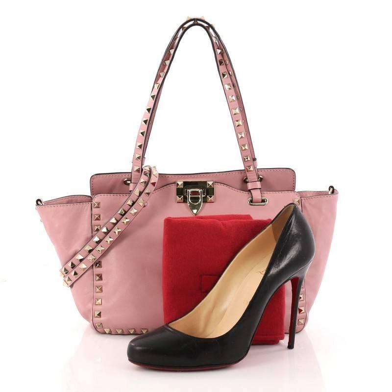 This authentic Valentino Rockstud Tote Soft Leather Small mixes edgy style with luxurious detailing. Crafted from pink soft leather, this stylish tote features dual tall flat handles, gold-tone pyramid stud trim details, a signature clasp fastening,