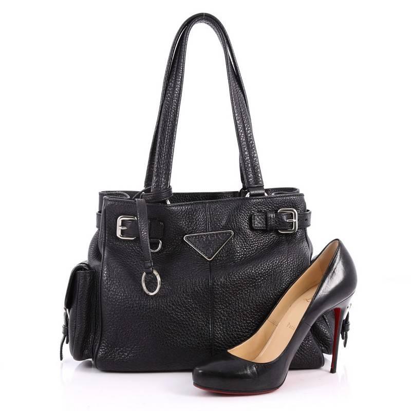 This authentic Prada Side Pocket Belt Tote Vitello Daino Medium is a spacious everyday bag. Crafted from nero black vitello daino leather, this tote features dual-flat handles, side strap buckles, side flap pockets, raised Prada logo at the center,