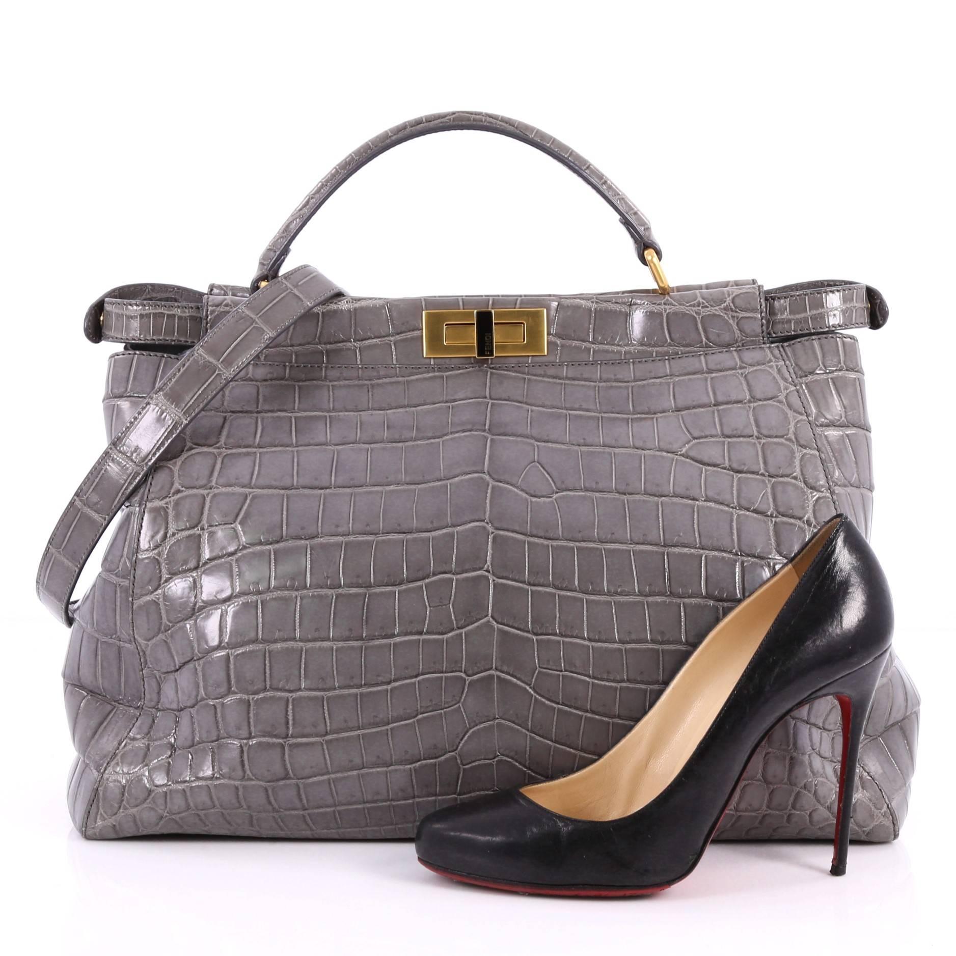 Diese authentische Fendi Peekaboo Handtasche Crocodile Large ist eines der bekanntesten Designs von Fendi und strahlt ein luxuriöses und dennoch minimalistisches Aussehen aus. Diese vielseitige und stilvolle Tasche aus echter grauer Krokodilleder