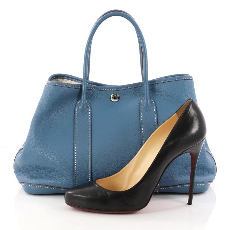This authentic Hermes Garden Party Tote Leather 30 is an elegant and simple tote made for all seasons. Crafted from blue jean leather, this chic everyday tote features dual-rolled leather top handles, palladium button closure, side snap buttons and