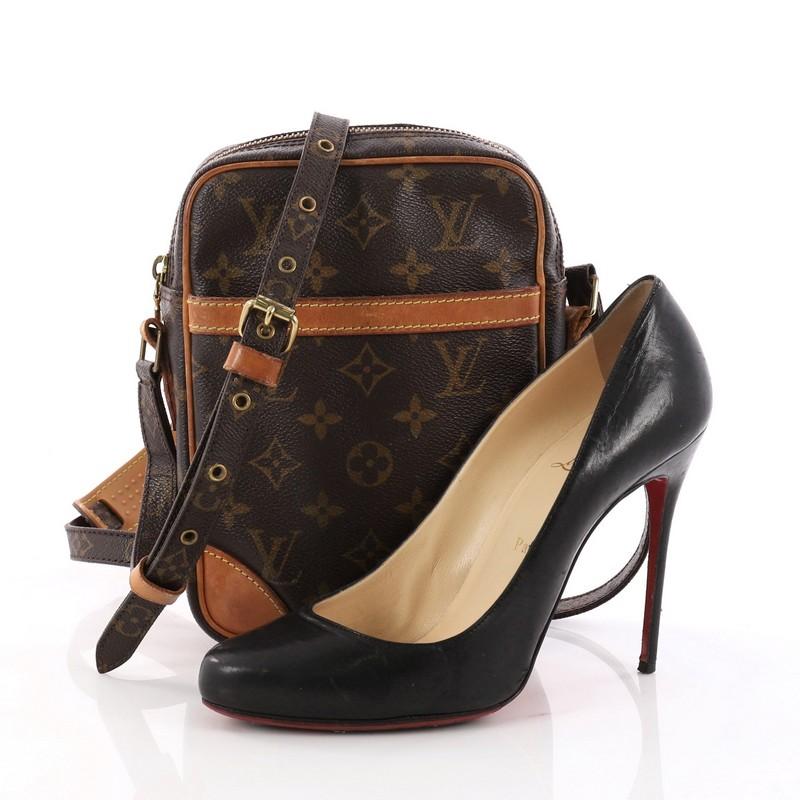 This authentic Louis Vuitton Danube Handbag Monogram Canvas is the perfect companion for traveling light and storing small essentials. Crafted in the brand's iconic brown monogram coated canvas, this small crossbody features vachetta leather trims,