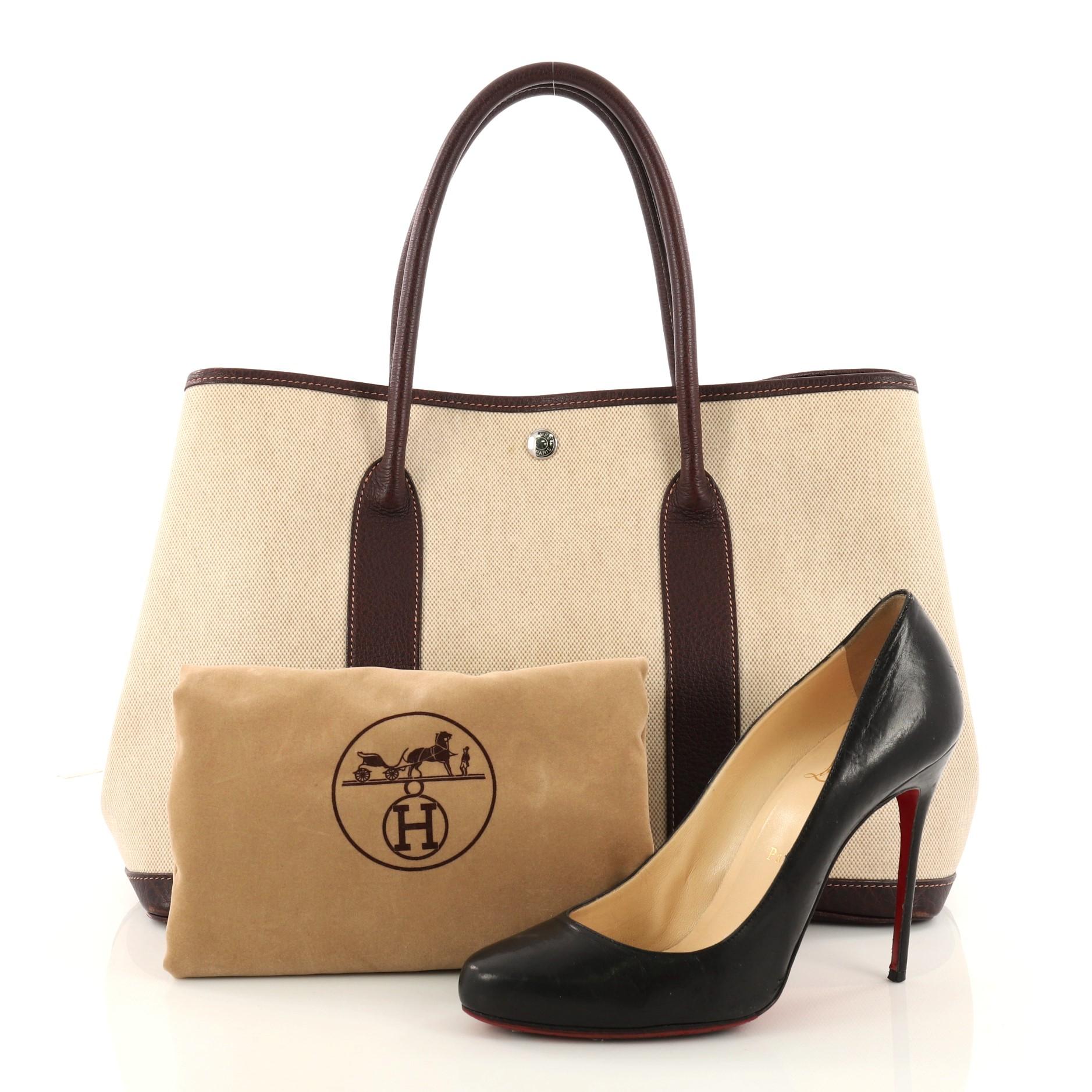 This authentic Hermes Garden Party Tote Toile and Leather 36 is an elegant and simple tote made for all seasons. Crafted from beige toile with wine buffalo leather trims, this chic everyday tote features dual-rolled leather top handles, stand-out