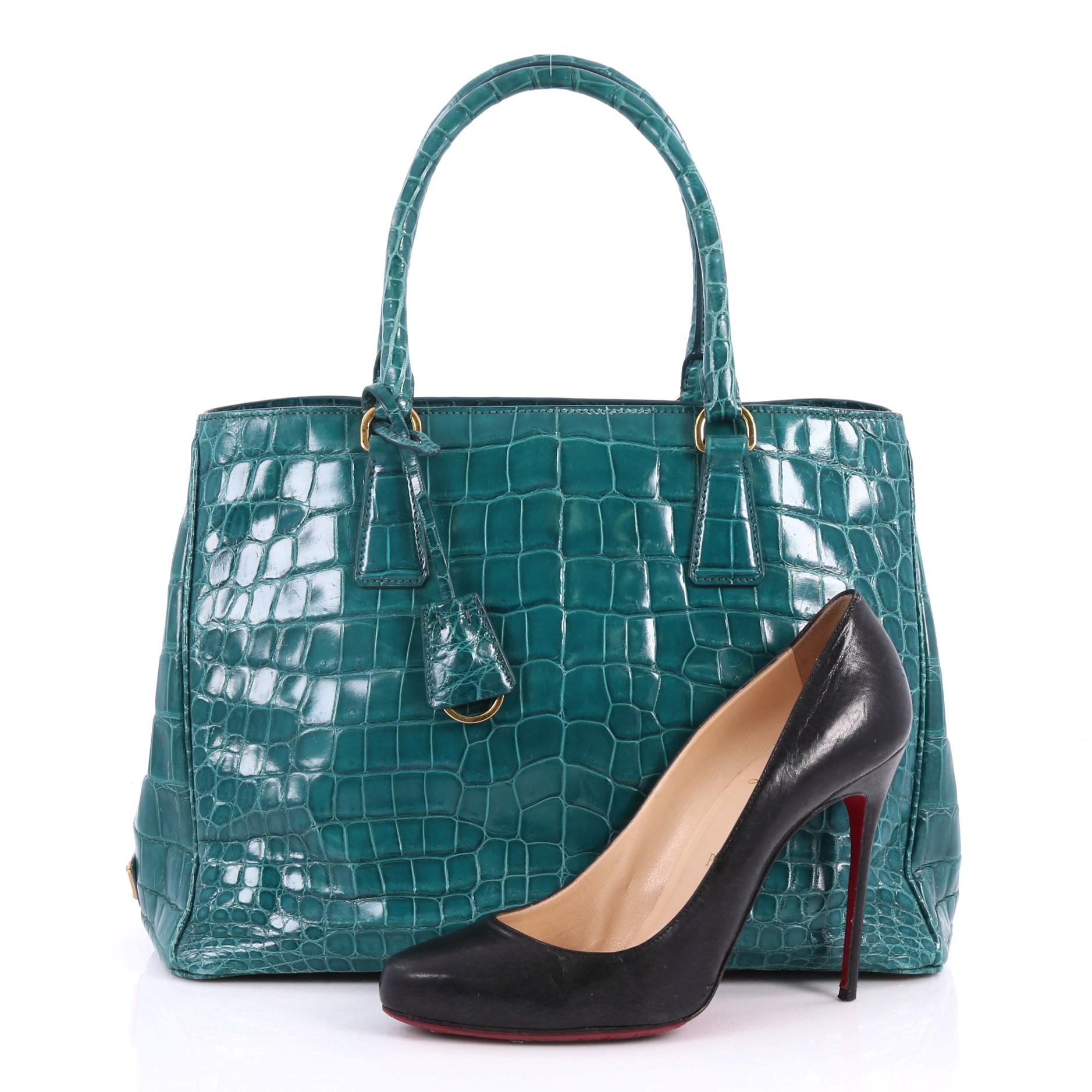 This authentic Prada Gardener's Tote Crocodile Medium is elegant in its simplicity and structure. Crafted from genuine green crocodile, this tote features dual-rolled leather handles, signature Prada logo on the side, protective base studs, and