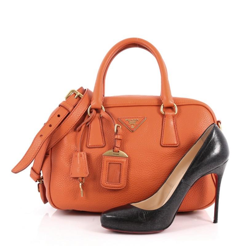 This authentic Prada Convertible Bauletto Bag Vitello Daino Small exudes a stylish and industrial design made for everyday excursions. Crafted from orange vitello daino leather, this exquisite bag features dual-rolled handles, raised Prada Milano