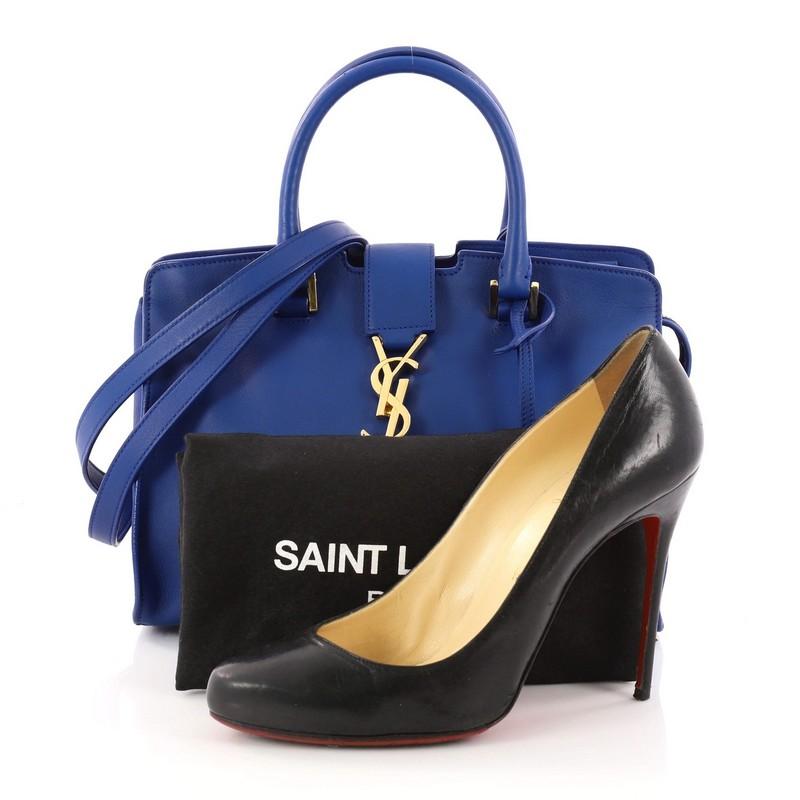 This authentic Saint Laurent Monogram Cabas Leather Baby combines a modern and functional style with an edgy twist. Crafted from blue leather, this boxy, satchel features dual-rolled handles, YSL metal logo at the front, protective base studs and