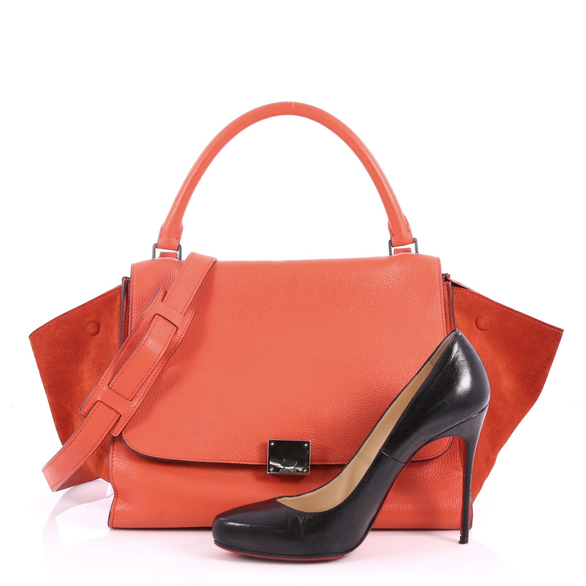 This authentic Celine Trapeze Handbag Leather Medium is a modern minimalist design with a playful twist in an array of subdued colors. Crafted from orange leather with orange suede wings, this popular bag features exterior back zip pocket, side snap