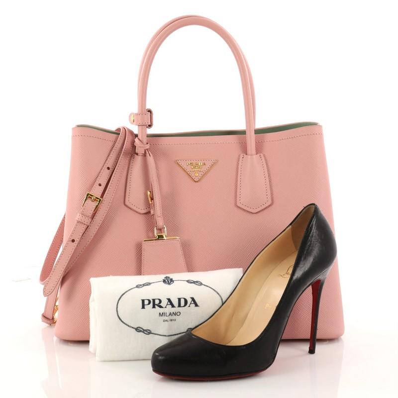 This authentic Prada Cuir Double Tote Saffiano Leather Small updates its popular Cuir line with a fresh, twist. Crafted from pink saffiano leather, this luxurious tote features dual-rolled top handles, side snap buttons, Prada's trademark triangle