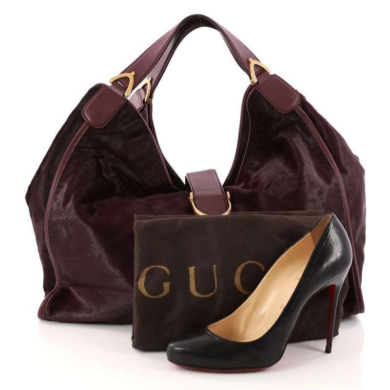 This authentic Gucci Soft Stirrup Tote Calf Hair Large in luxurious and sleek design is made for all seasons. Crafted in burgundy calf hair, this bag features side to side looped dual-flat handles with unique spur detailing and gold-tone hardware