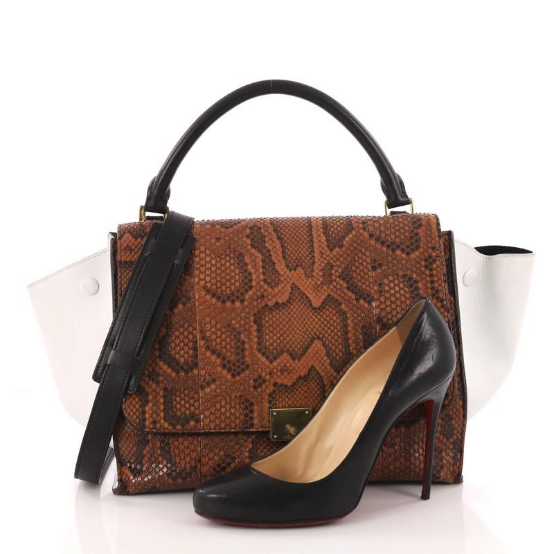 This authentic Celine Trapeze Handbag Python Medium is a fashionista's dream. Crafted in genuine brown python skin with white leather wings, this stylish bag features exterior back zip pocket, top handle and gold-tone hardware accents. Its square