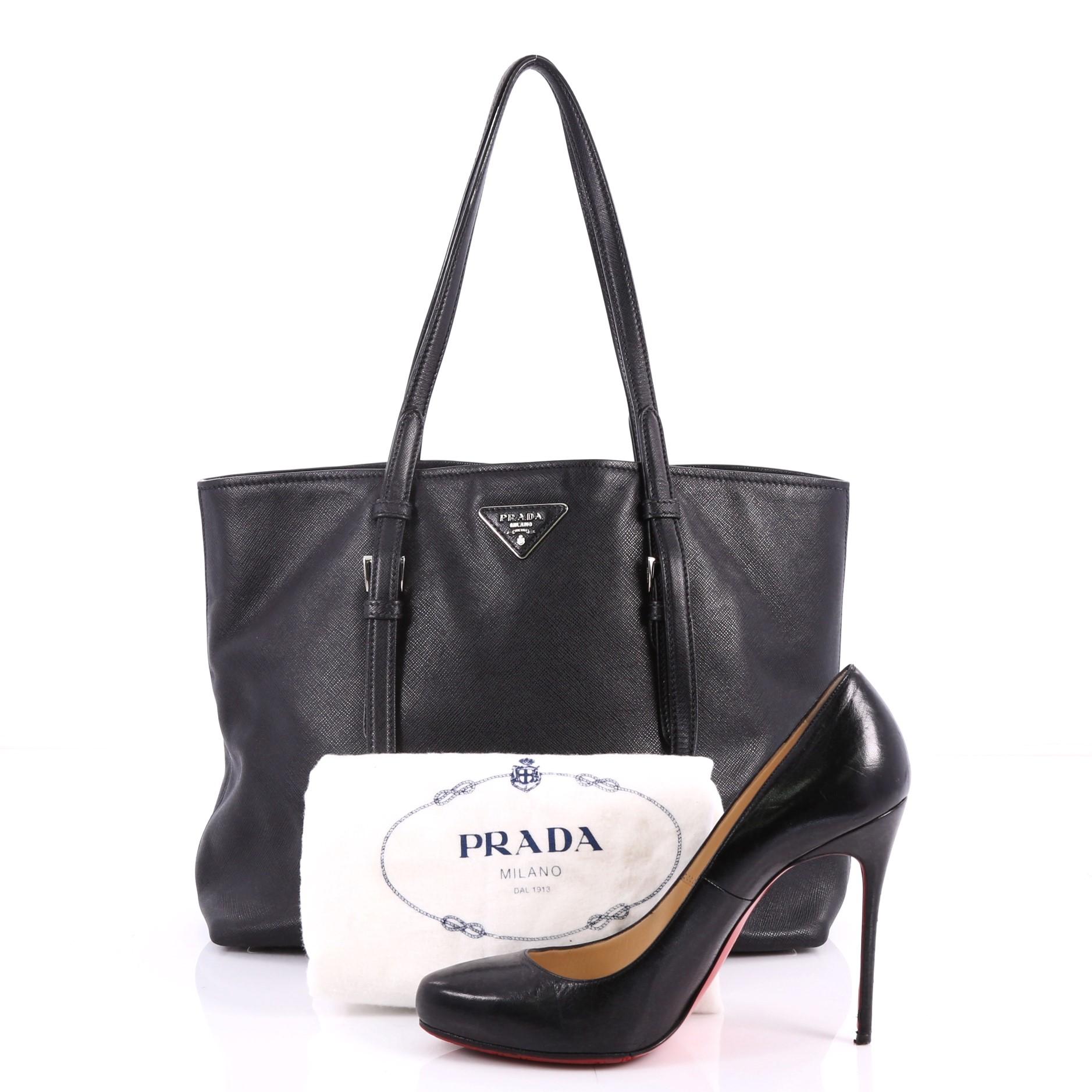 This authentic Prada Belted Soft Tote Saffiano Leather Medium is elegant in its simplicity and structure. Crafted in black saffiano leather, this stylish yet functional tote features dual slim leather handles with belt and buckle details, protective