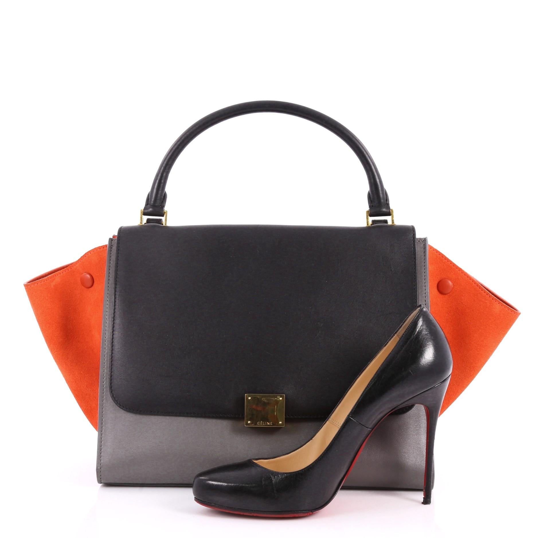 This authentic Celine Tricolor Trapeze Handbag Leather Medium is a modern minimalist design with a playful twist in an array of subdued colors. Crafted from black and gray leather and orange suede wings, this classic satchel features gold-tone