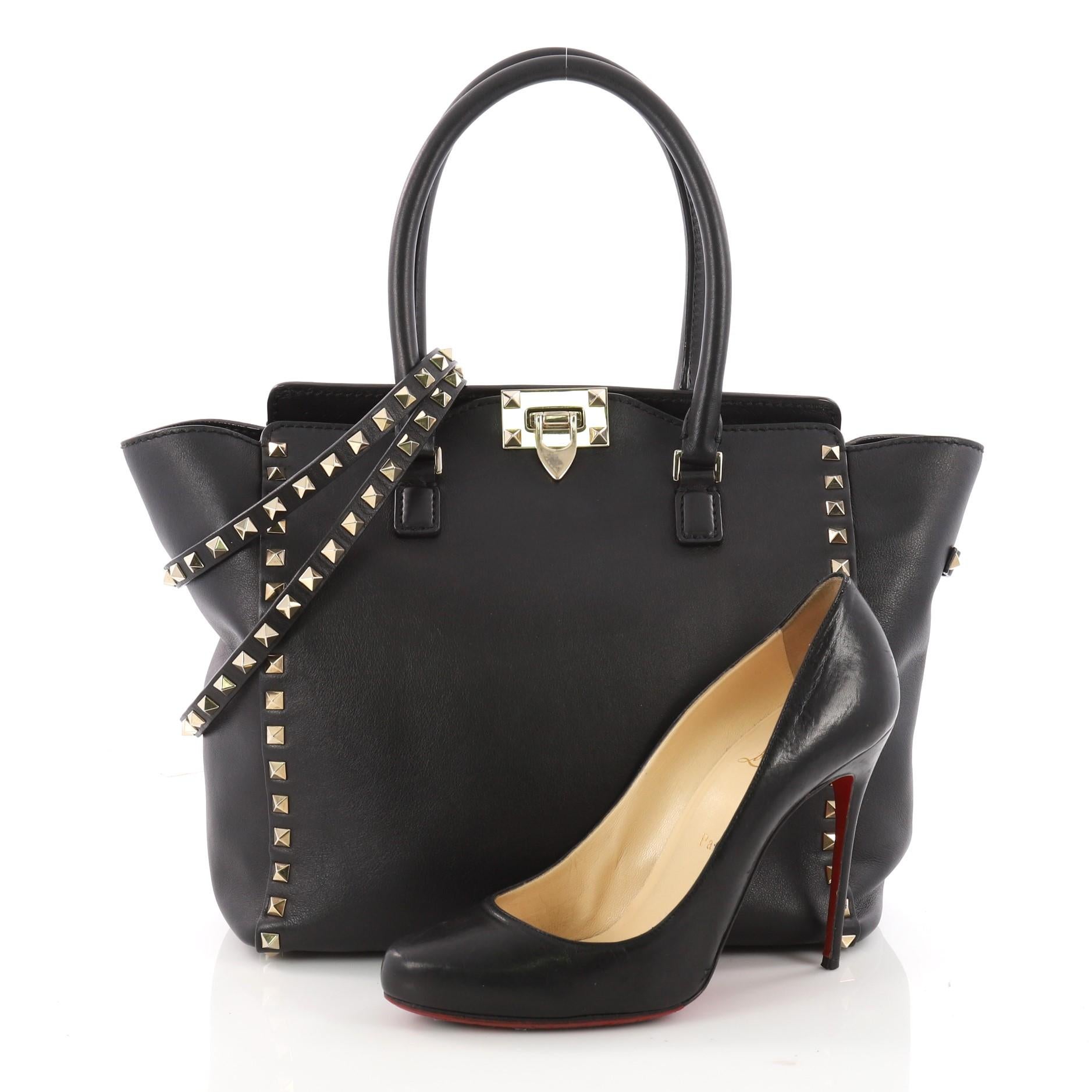 This authentic Valentino Rockstud Tote Rigid Leather Medium is a stylish and iconic bag that is one of today's most sought-after styles. Crafted from beautiful black rigid leather, this chic tote features signature gold pyramid stud borders,