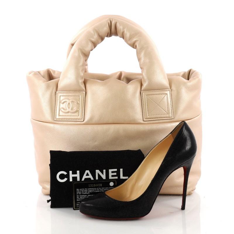 This authentic Chanel Coco Cocoon Reversible Tote Quilted Lambskin Small is a highly sought-after piece from Lagerfeld's fun and chic Coco Cocoon line. Crafted from gold-tone lambskin, this sporty tote features padded top handles, interlocking CC