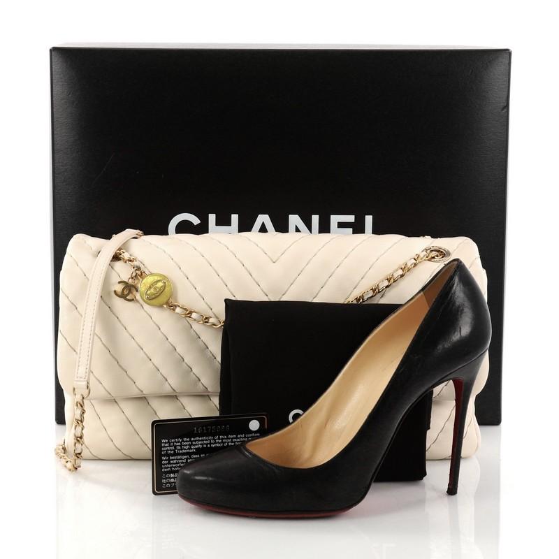 This authentic Chanel Medallion Charm Flap Bag Chevron Calfskin Jumbo presented in the brand's Cruise 2013-2014 Collection mixes feminine luxurious with casual youthfulness made for the modern woman. Crafted in luxurious off-white calfskin leather,