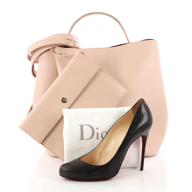 This authentic Christian Dior Diorific Bucket Bag Leather Small is a luxurious piece from Dior. Crafted in light pink leather, this chic bag features a single flat metal-embellished top handle and gold-tone hardware accents. Its snap closure opens