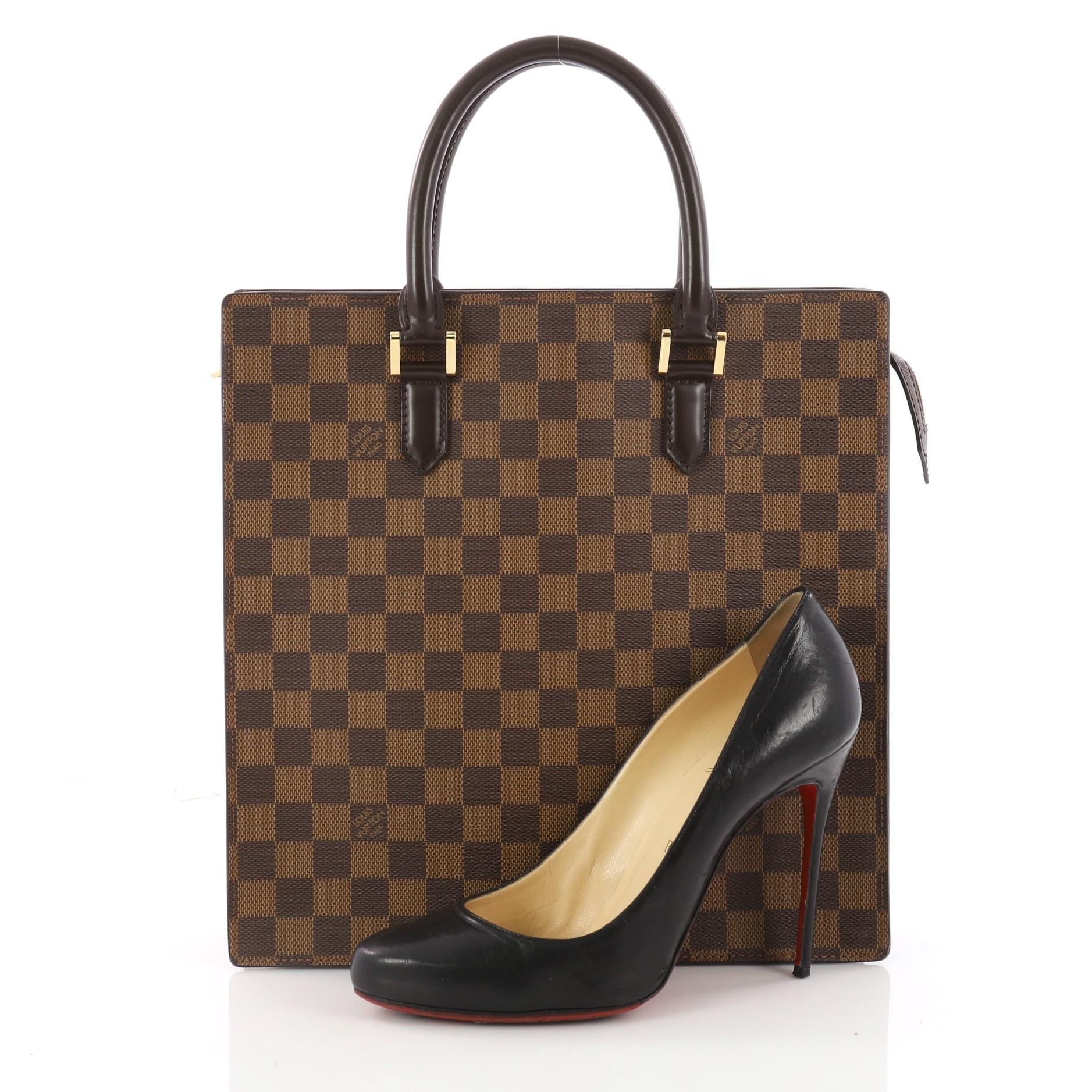 This authentic Louis Vuitton Venice Sac Plat Handbag Damier PM is a structured design perfect for everyday use. Crafted in iconic damier ebene coated canvas, this bag features simple shopper silhouette and dual-rolled leather handles. Its top zipper