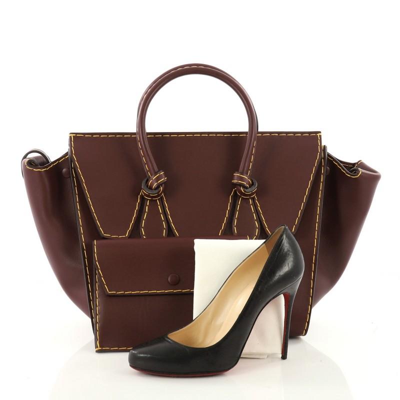 This authentic Celine Tie Knot Tote Smooth Leather Small is an absolute must-have for modern fashionistas. Crafted from burgundy smooth leather, this boxy, chic tote features dual-rolled leather handles with signature knot accents, protective base