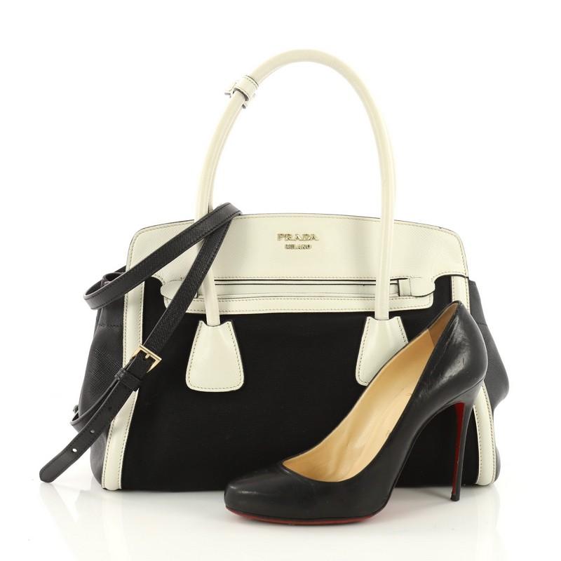 This authentic Prada Frame Tote Canvas and Saffiano Leather is a bag elegant in its simplicity and structure. Crafted in black canvas and white saffiano leather trim, this frame tote features dual-rolled handles, protective base studs, side snap