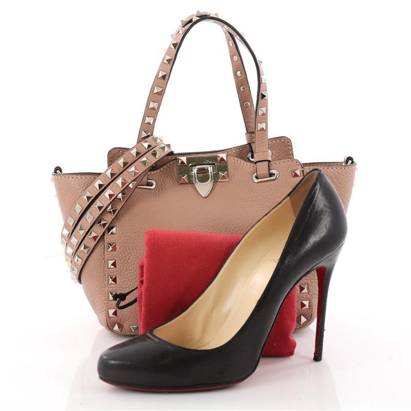 This authentic Valentino Rockstud Tote Pebbled Leather Mini is a stylish and iconic tote that is one of today's most sought-after styles. Crafted from dark mauve pink pebbled leather, this stand-out tote features signature gold pyramid stud border