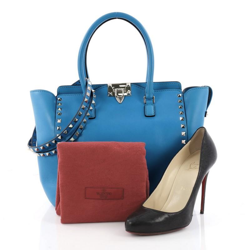 This authentic Valentino Rockstud Tote Rigid Leather Medium is a stylish and iconic bag that is one of today's most sought-after styles. Crafted from beautiful blue rigid leather, this chic tote features signature gold pyramid stud borders,