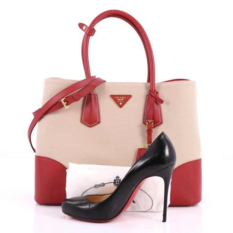 This authentic Prada Cuir Double Tote Canvas and Saffiano Leather Medium is elegant in its simplicity and structure. Crafted from sturdy beige canvas and red saffiano leather, this tote features dual-rolled handles, side snap buttons, Prada's