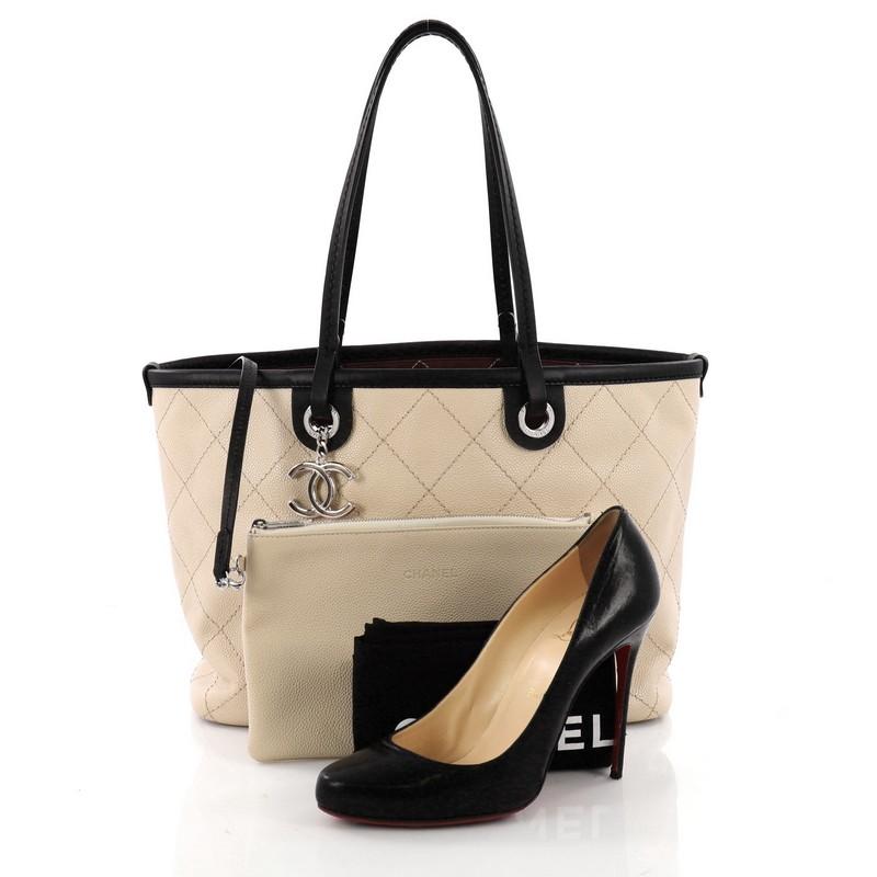 This authentic Chanel Fever Tote Quilted Caviar Small is perfect for everyday use. Crafted from beige quilted caviar leather, this lightweight tote features dual flat leather handles, smooth leather trims, CC silver charm, protective base studs and