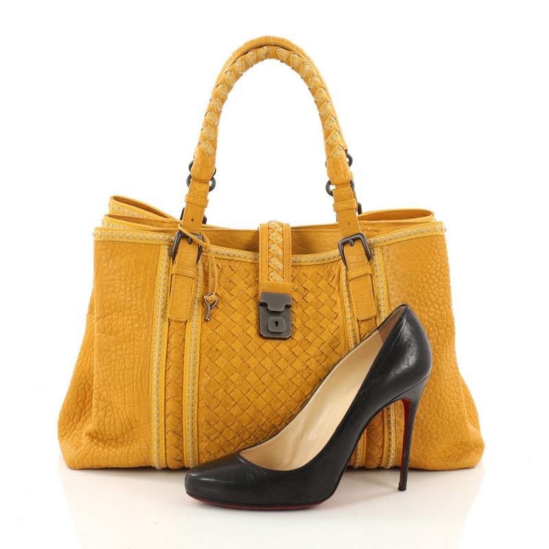This authentic Bottega Veneta Roma Handbag Leather with Intrecciato Detail Medium is a finely crafted tote that exudes an understated elegance. Crafted from mustard leather with intrecciato detailing, it features dual woven leather handles with