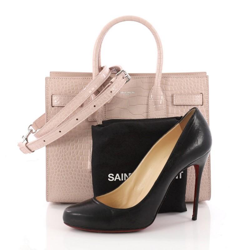 This authentic Saint Laurent Sac de Jour NM Handbag Crocodile Embossed Leather Baby is a sleek and elegant bag, representative of the brand's classic aesthetic. Crafted from pink crocodile embossed leather, this sought-after structured tote features