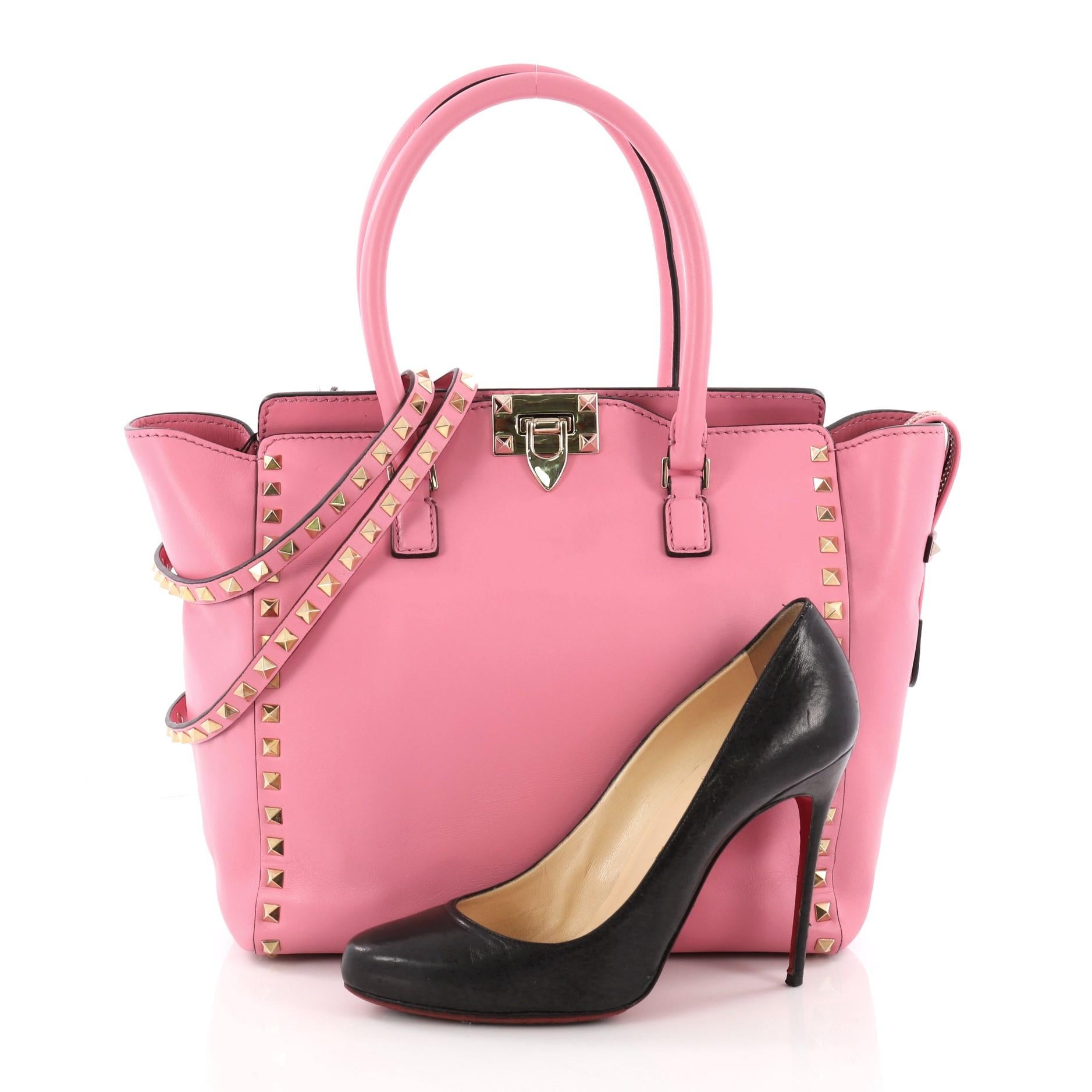 This authentic Valentino Rockstud Tote Rigid Leather Medium is a stylish and iconic bag that is one of today's most sought-after styles. Crafted from beautiful pink rigid leather, this chic tote features signature gold pyramid stud border,
