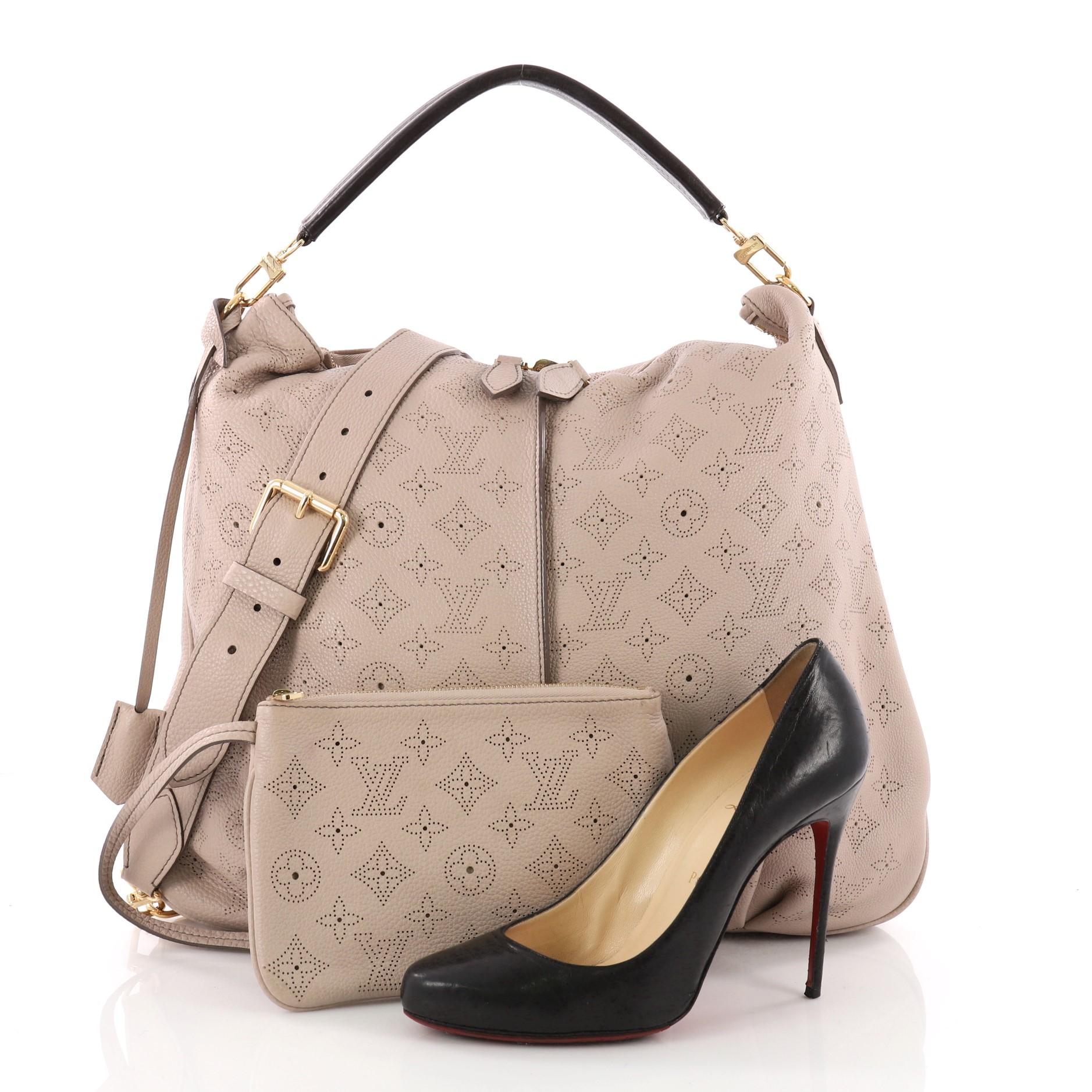 This authentic Louis Vuitton Selene Handbag Mahina Leather MM is a feminine design. Crafted from taupe monogram perforated mahina leather, this beautiful hobo features pleated detailing and gold-tone hardware accents. Its top zip closure opens to a