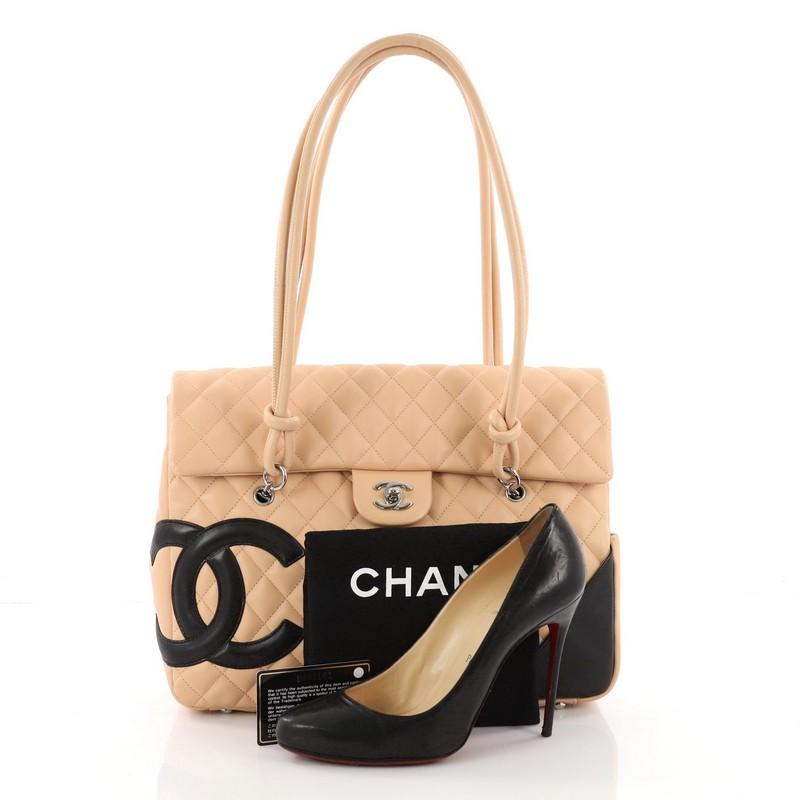 This authentic Chanel Cambon Flap Tote Quilted Leather Large is a stylish and functional accessory perfect for daily excursions. Crafted in nude quilted leather, this tall tote features tall, looping shoulder straps with knotted ends, signature CC