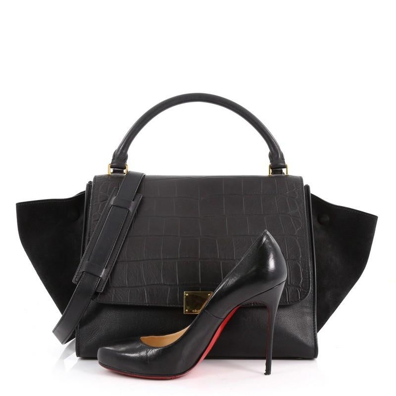 This authentic Celine Trapeze Handbag Crocodile Embossed Leather Medium is a fashionista's dream bag. Crafted from black crocodile embossed leather with black suede wings, this bag features top rolled leather handle, side wings snap closures, zip