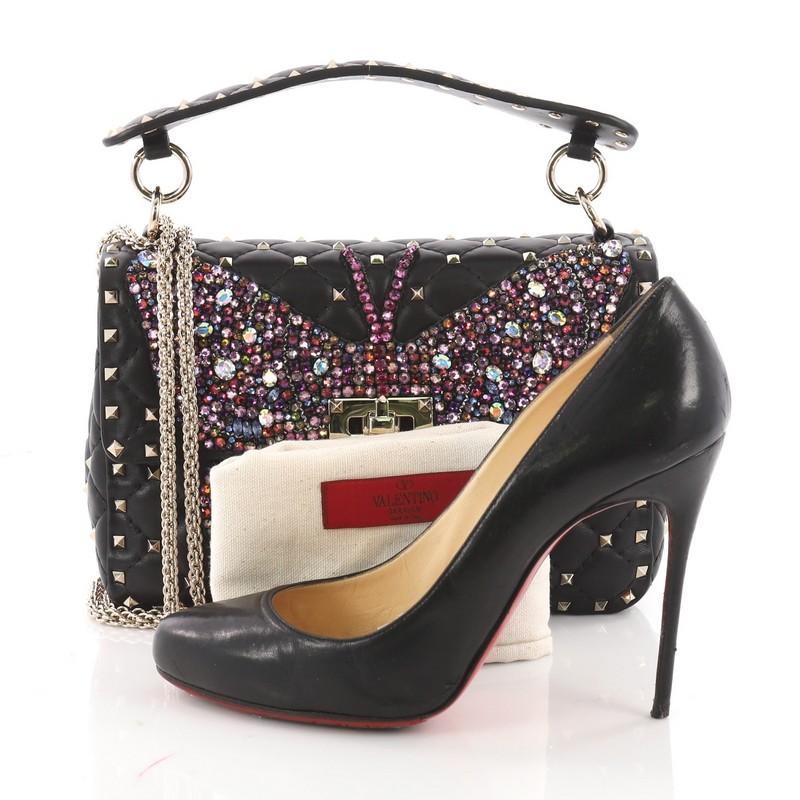 This authentic Valentino Rockstud Spike Flap Bag Crystal Embellished Quilted Leather Medium is an exquisitely made bag that brings a hit of glamour to your endless looks. Crafted from black crystal embellished quilted leather, this edgy and stylish