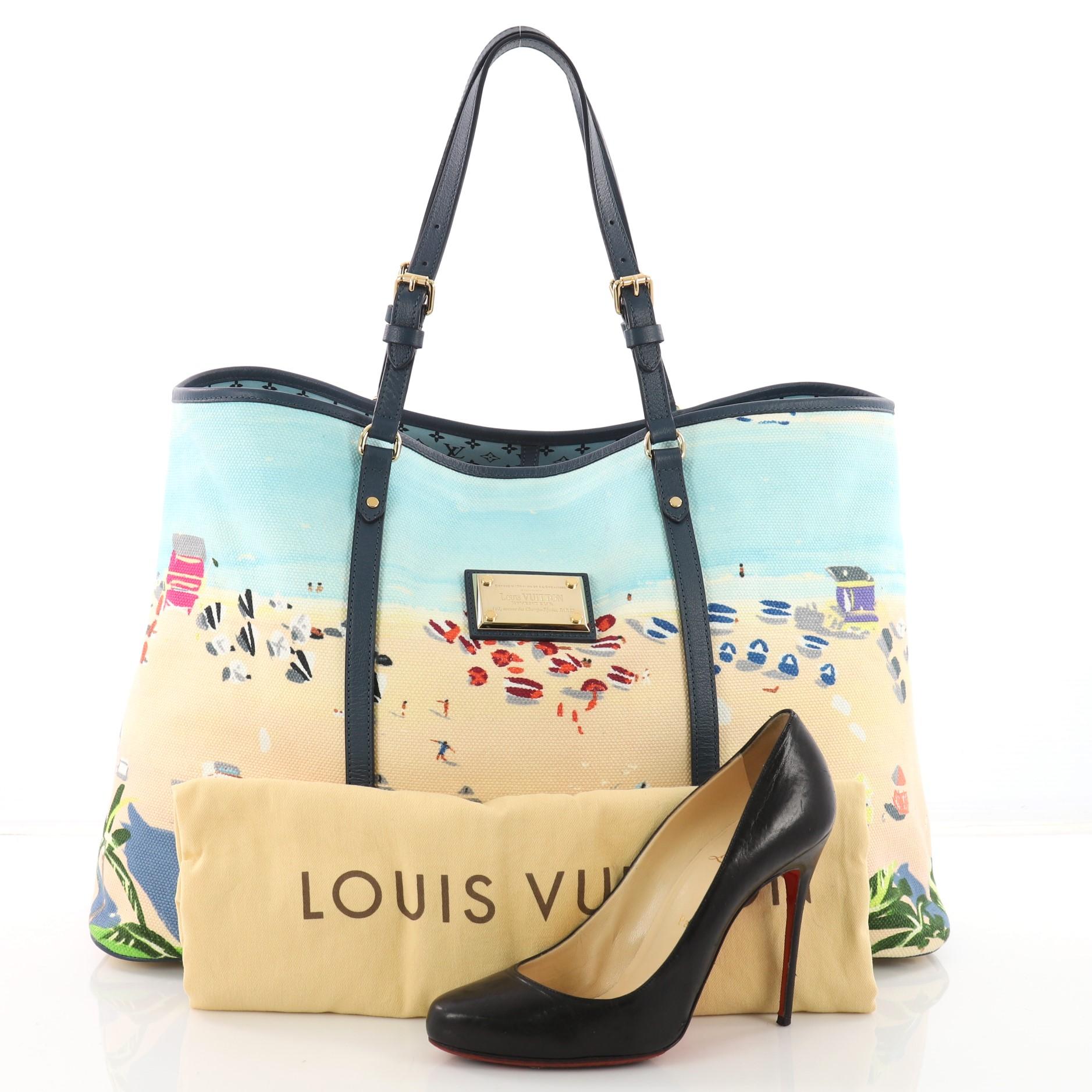 This authentic Louis Vuitton Ailleurs Cabas Limited Edition Printed Canvas GM is inspired by the eternal allure of white sand, turquoise sea and lazy hours spent reading under a brightly colored beach umbrella. Crafted from blue printed canvas, this