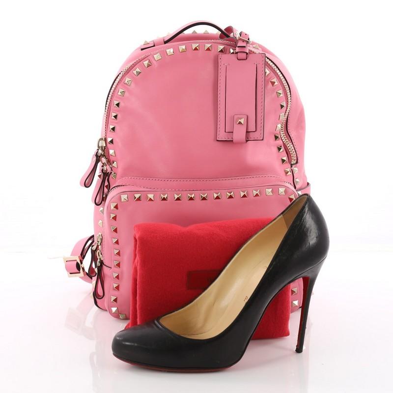 This Valentino Rockstud Backpack Leather Medium, crafted from pink leather, features adjustable backpack straps, rockstud trim, and gold-tone hardware accents. Its zip closure opens to a tan fabric-lined interior with slip pocket. **Note: Shoe