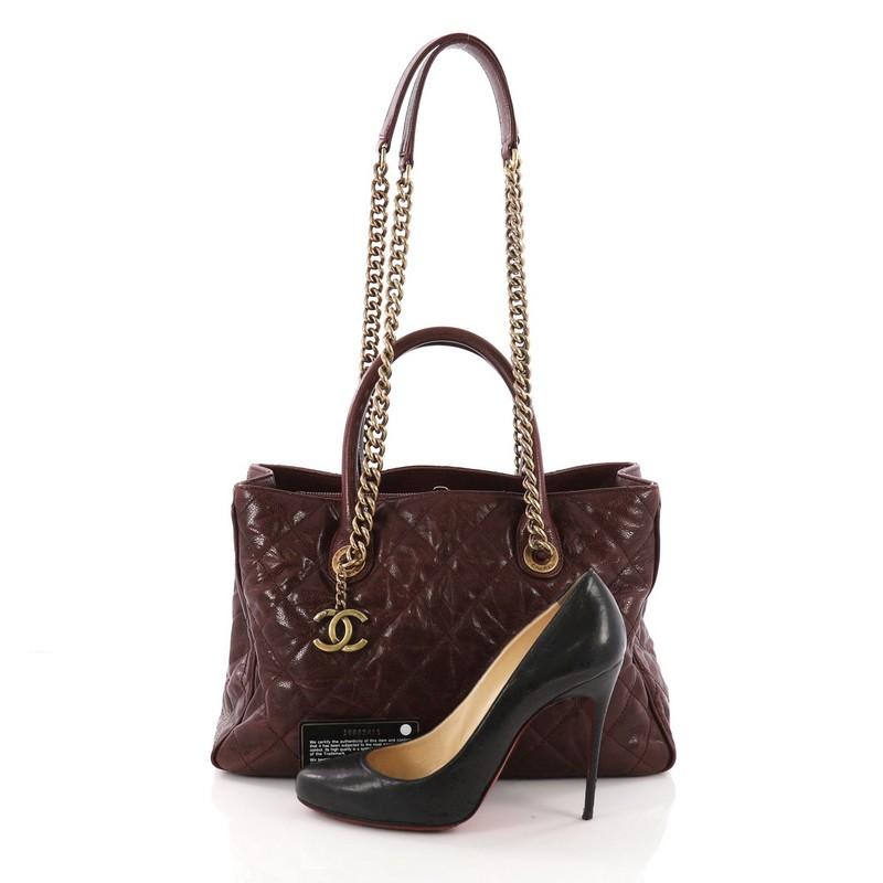 This Chanel Shiva Tote Quilted Caviar Medium, crafted from burgundy quilted caviar leather, features dual-rolled leather handles, chunky aged gold chain link straps with shoulder pads, and aged gold-tone hardware. Its open top showcases a burgundy