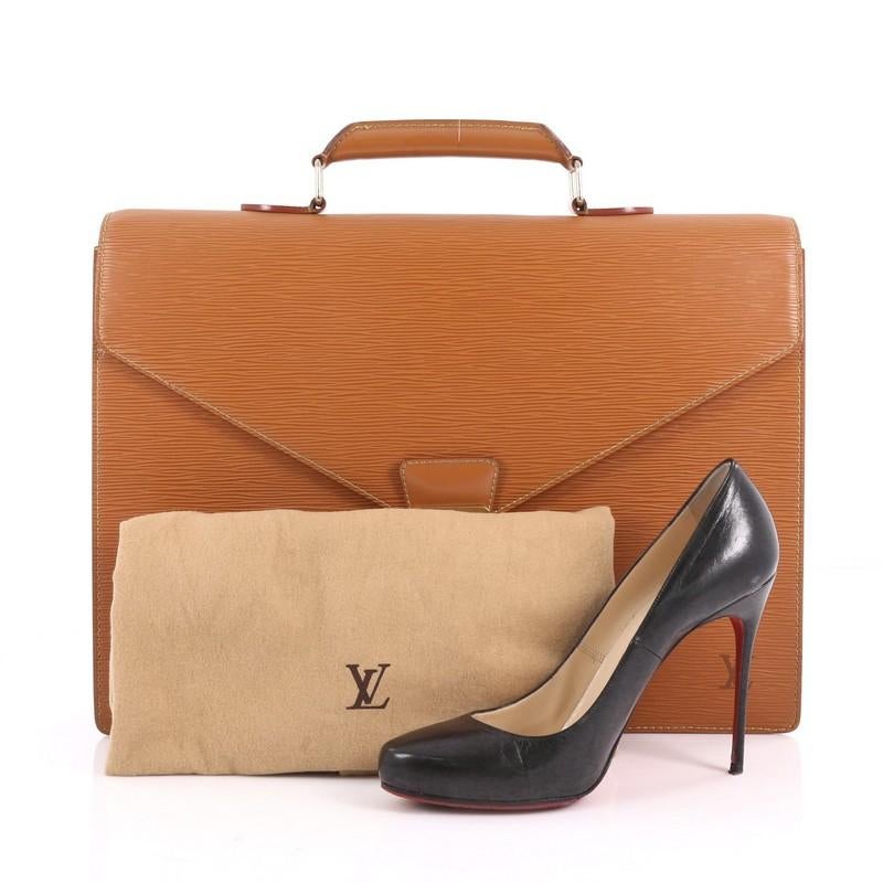 This Louis Vuitton Serviette Ambassadeur Handbag Epi Leather, crafted in brown epi leather, features a top handle, back slip pocket and gold-tone hardware. Its S-lock closure opens to a brown leather interior divided into two open compartments with