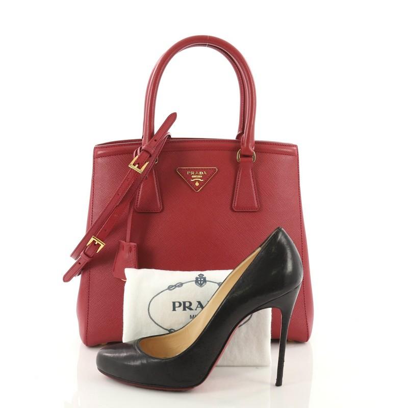 This Prada Lux Convertible Open Tote Saffiano Leather Small, crafted from red saffiano leather, features dual-rolled handles, iconic inverted Prada triangle logo at the center, and gold-tone hardware accents. Its magnetic snap closure opens to a red