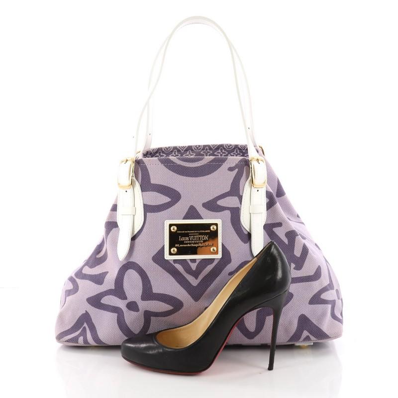 This Louis Vuitton Tahitienne Cabas Canvas PM, crafted from purple canvas, features adjustable white leather handles with buckle detailing, hand-painted effect monogram print, and gold-tone hardware accents. Its wide top opening displays a purple