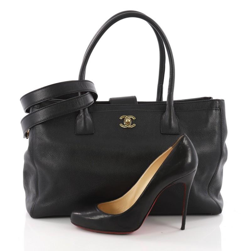 This Chanel Cerf Executive Tote Leather Medium, crafted from black leather, features dual rolled tall handles, front pocket with CC turn-lock closure and gold-tone hardware. Its top magnetic snap closure opens to a black fabric interior with zip