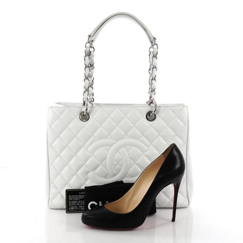 This Chanel Grand Shopping Tote Quilted Caviar, crafted in white quilted caviar leather, features woven-in leather chain straps with leather pads, exterior back pocket, and silver-tone hardware. It opens to a gray satin interior with two open