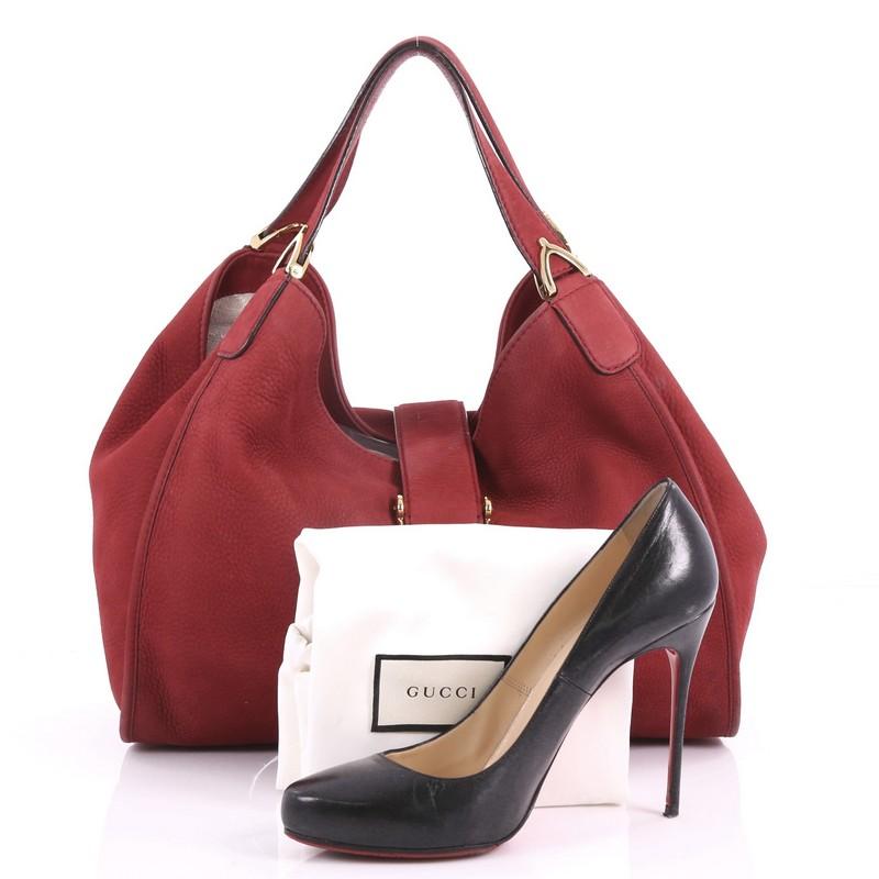 This Gucci Soft Stirrup Tote Nubuck Medium, crafted from dark red nubuck, features side to side looped dual flat handles with spur detailing and gold-tone hardware. Its slide flap closure opens to a beige fabric interior with side zip and slip