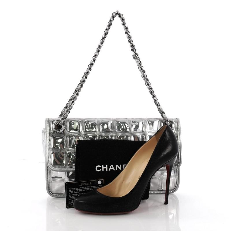 This Chanel Ice Cube Flap Bag Quilted Vinyl, crafted from silver quilted vinyl, features a unique ice cube design, woven-in leather chain strap and gunmetal-tone hardware accents. Its CC turn-lock closure opens to a gray fabric interior with side