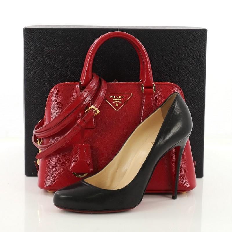 This Prada Promenade Handbag Vernice Saffiano Leather Small, crafted from red vernice saffiano leather, features dual rolled handles, signature triangle Prada logo, and gold-tone hardware. Its two-way zip closure opens to a red fabric interior with
