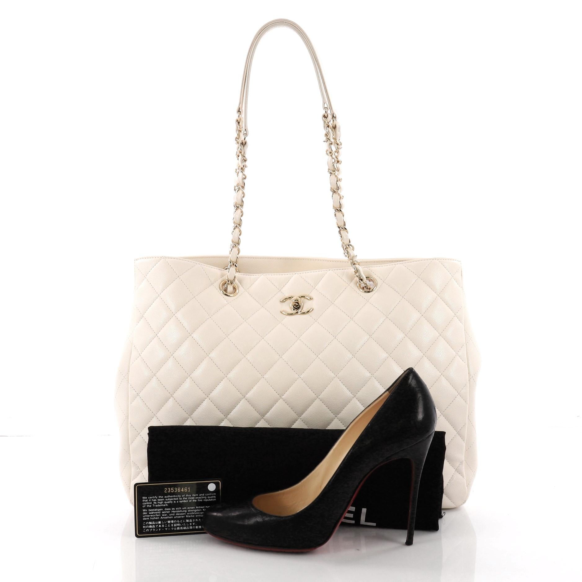 This Chanel Classic CC Shopping Tote Quilted Caviar Large, crafted from off-white quilted caviar leather, features woven-in leather chain straps with leather shoulder pads, exterior back slip pocket, side snap buttons and gold-tone hardware. Its CC