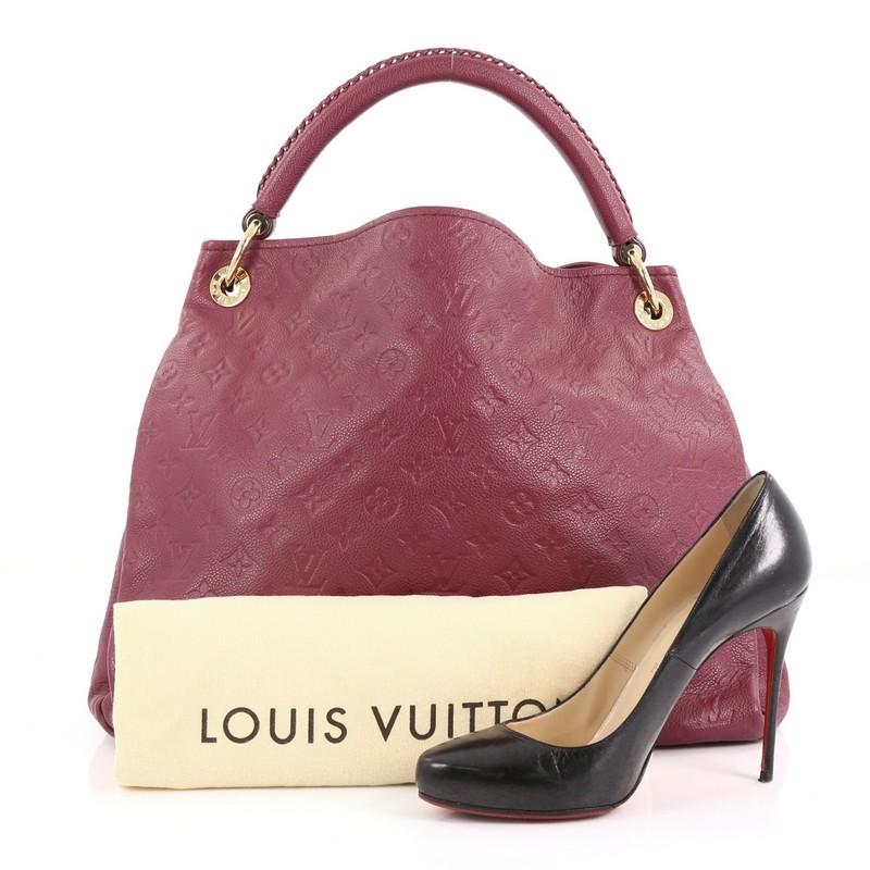 This Louis Vuitton Artsy Handbag Monogram Empreinte Leather MM, crafted from berry monogram embossed empreinte leather, features a braided handle with polished gold links, and gold-tone hardware. Its wide open top showcases a roomy berry fabric